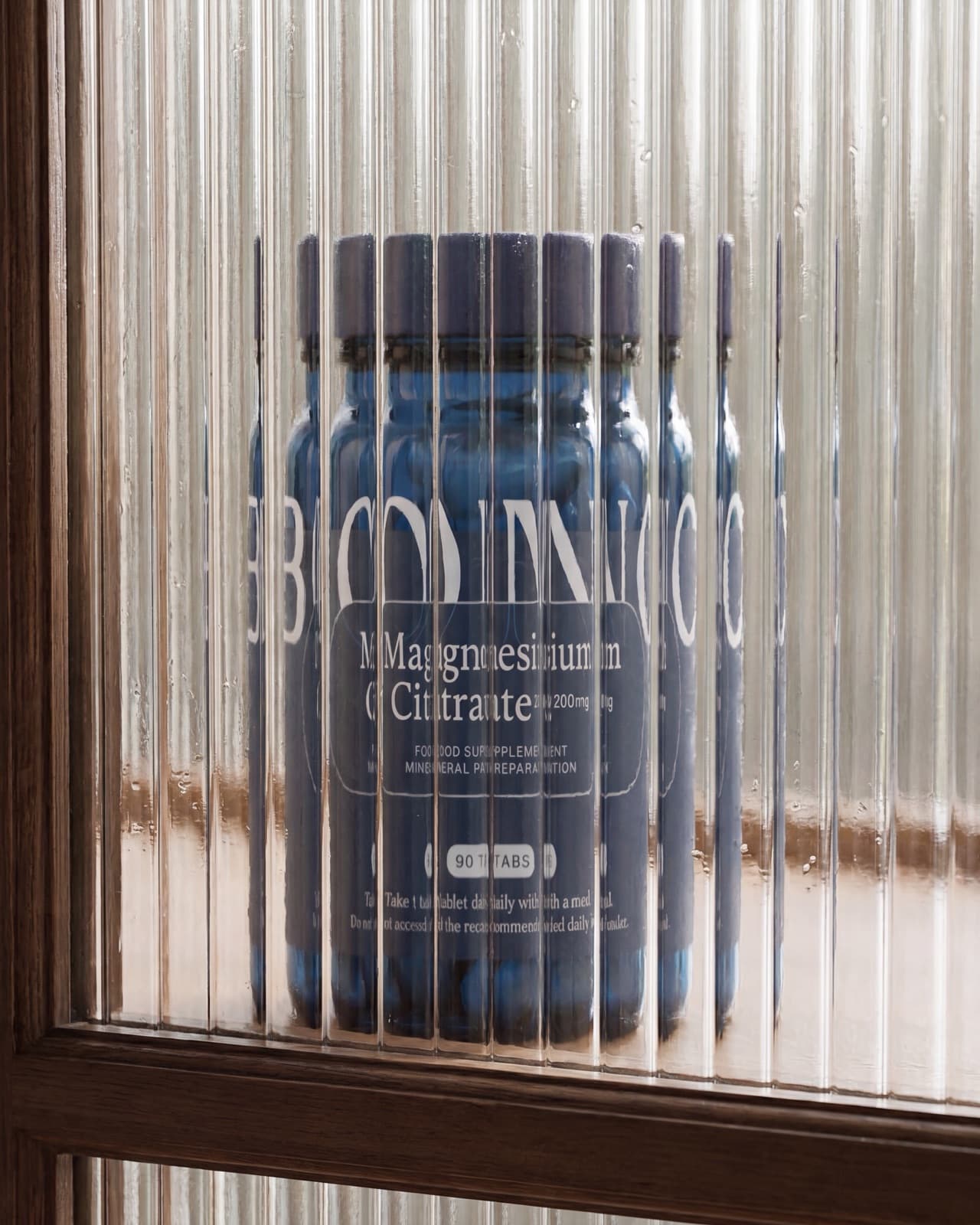 Eine Dose BONO Supplements Magnesiumcitrat hinter geriffeltem Glas